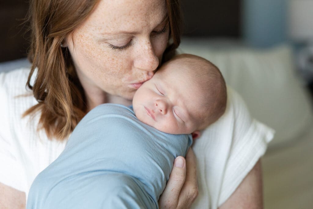 Mother giving a sweet kiss to her newborn baby boy's cheek.