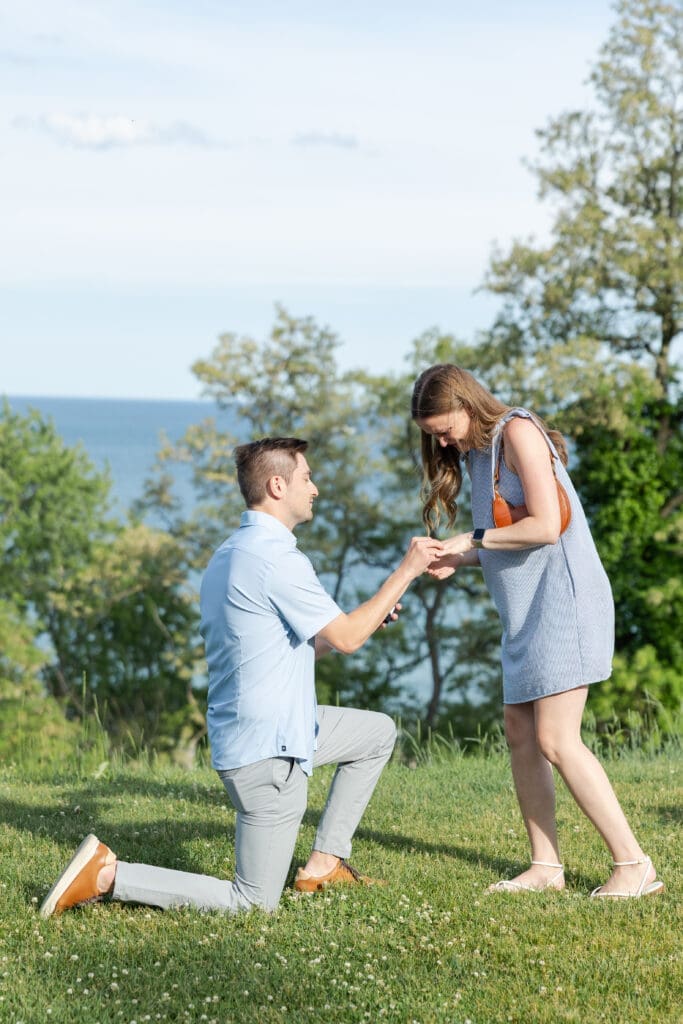 A man down on one knee proposing to his girlfriend overlooking Lake Michigan.