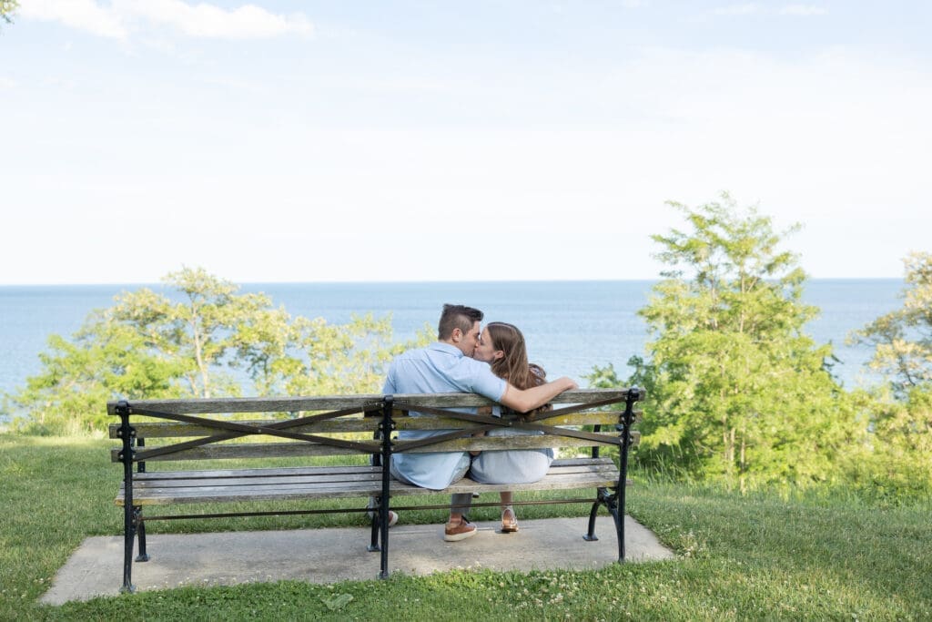 Engaged couple kissing on a park bench overlooking Lake Michigan.