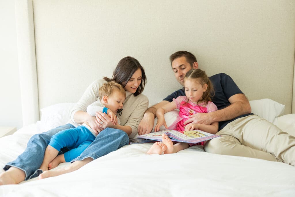 A mother and father with their two young children on their bed during an at-home family photography session in Milwaukee.
