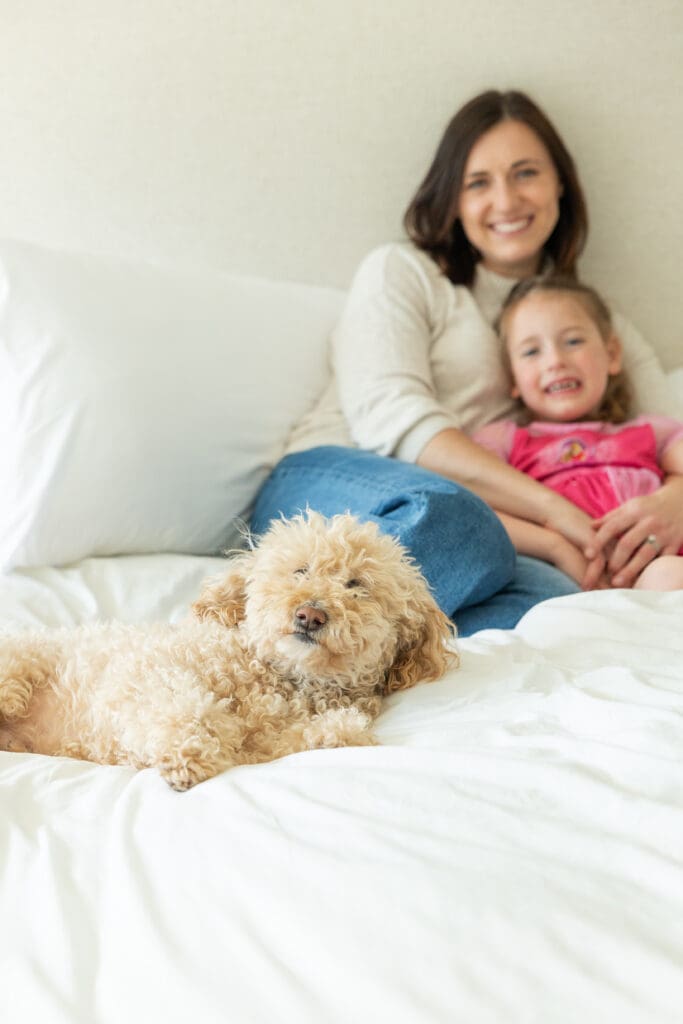 Mom and daughter relaxing on a bed while their family dog is close by.