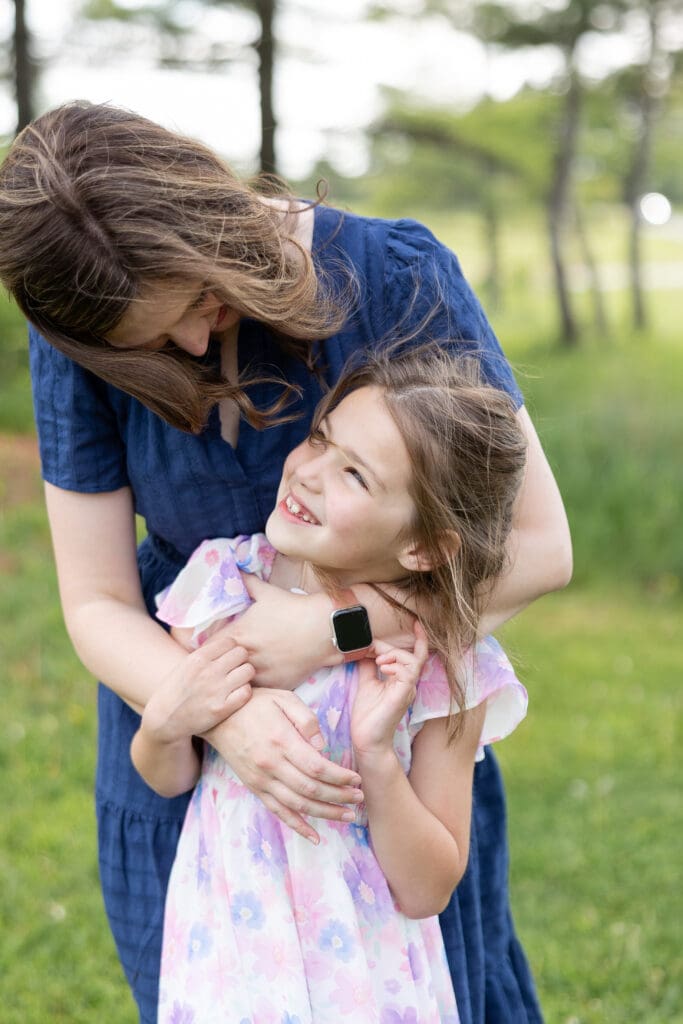 A young girl looks up at her mother smiling, both embracing and looking happy.