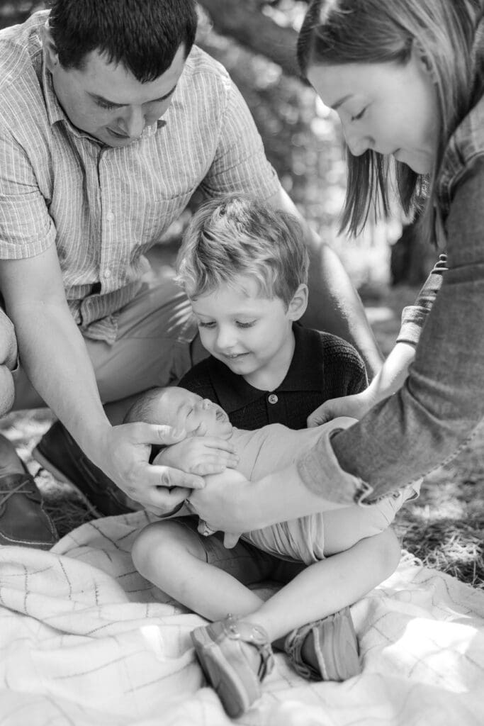 Parents helping their young son hold his new baby sister.