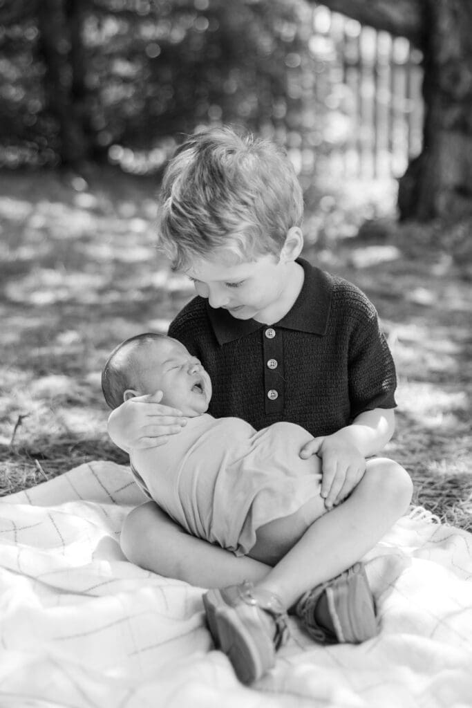 A proud new big brother holding his baby sister on his own during an at home photography session in MIlwaukee.