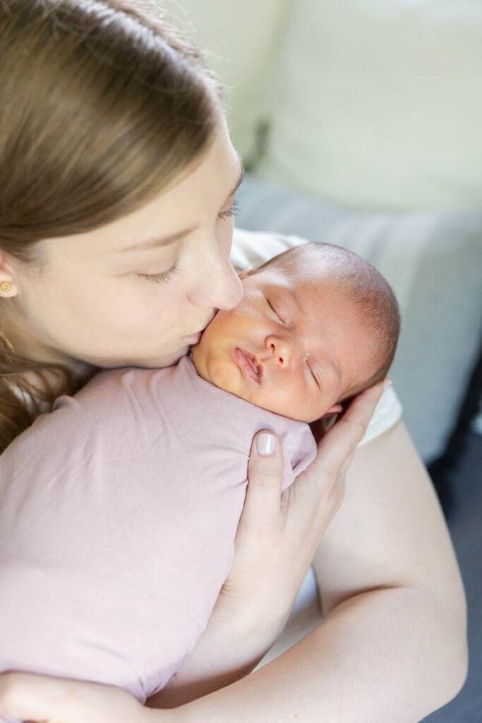 A mother kissing her swaddled newborn baby girl on the cheek.