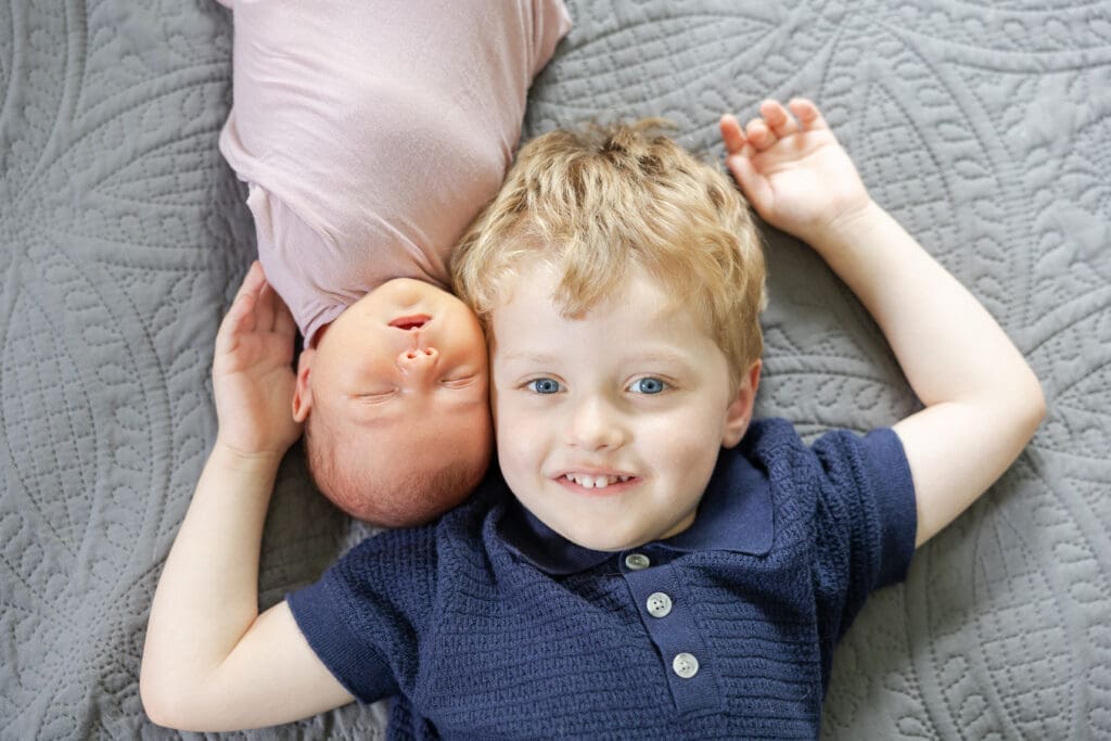 Newborn baby sister cheek to cheek with her big brother.