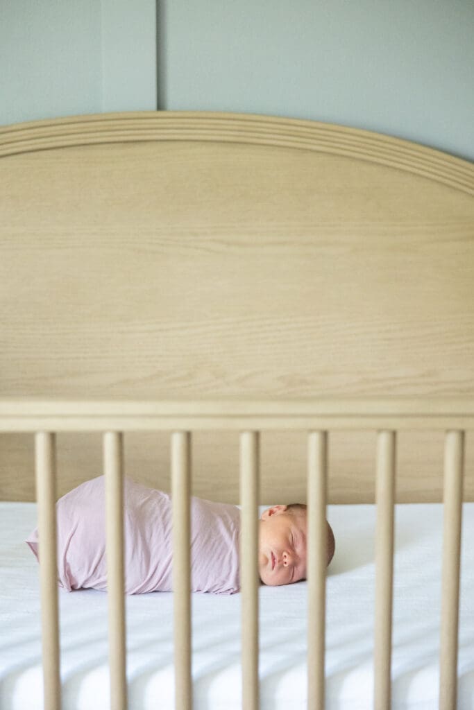 Sweet baby girl swaddled in pink sleeping sweetly in her modern wood crib.