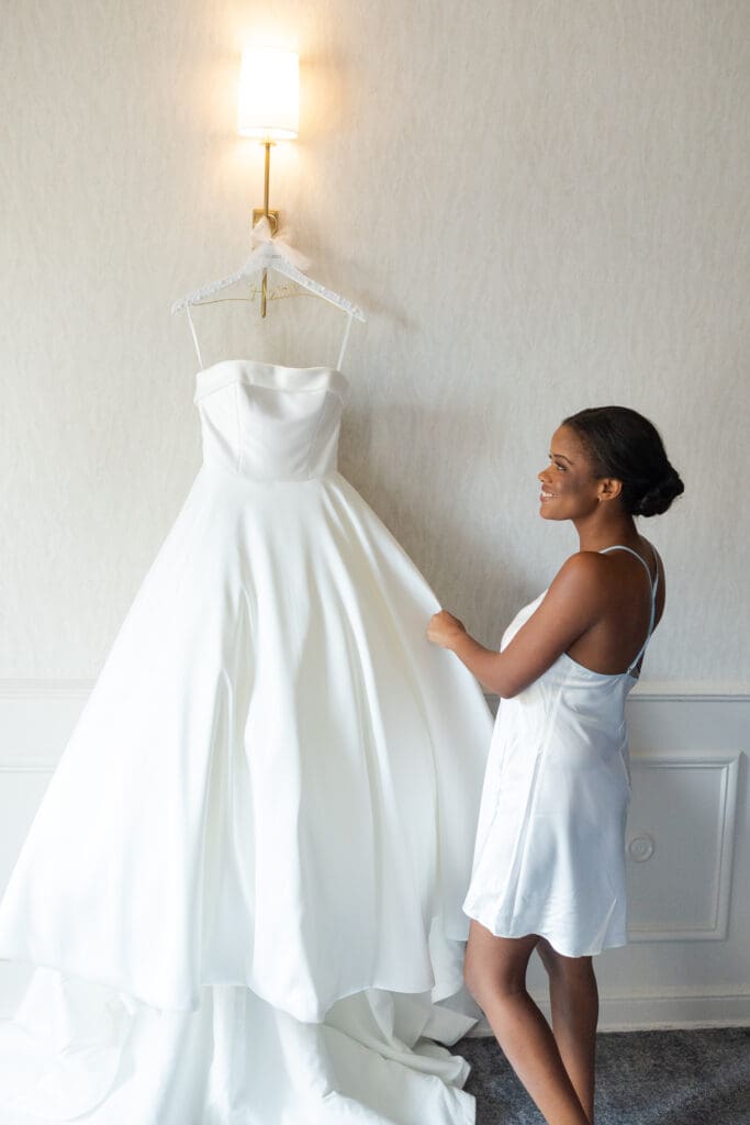 Bride looking at her wedding gown on a hanger before she gets dressed. 