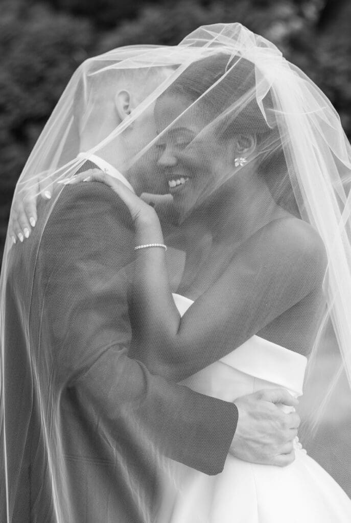 Bride and groom embracing while the bride's veil is covering them.