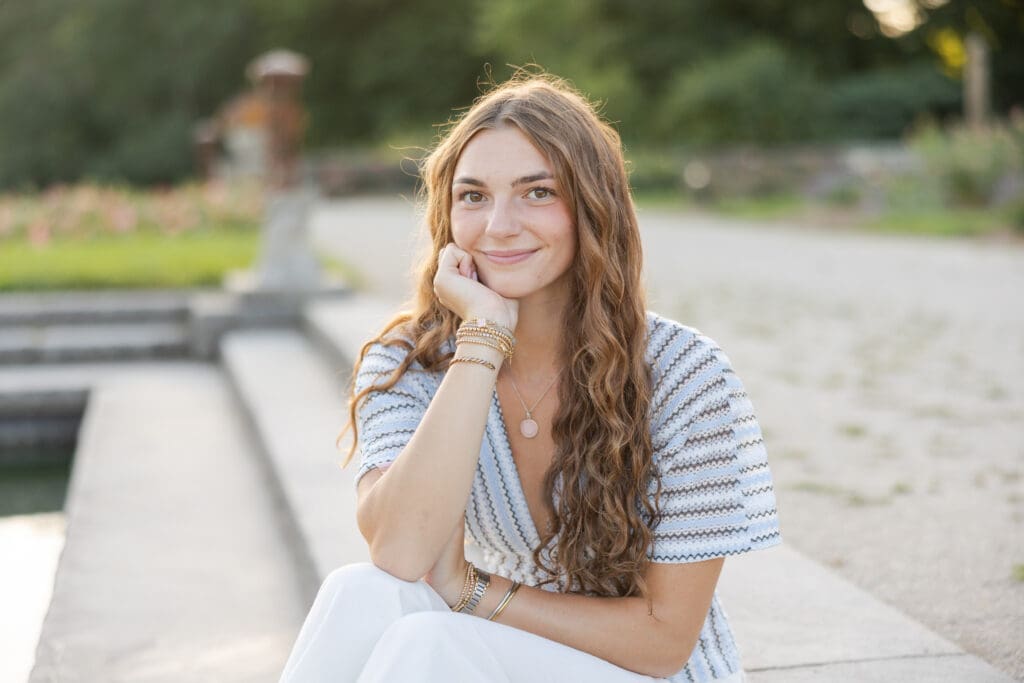Senior highschool girl smiling at the camera with her head resting in her hands.