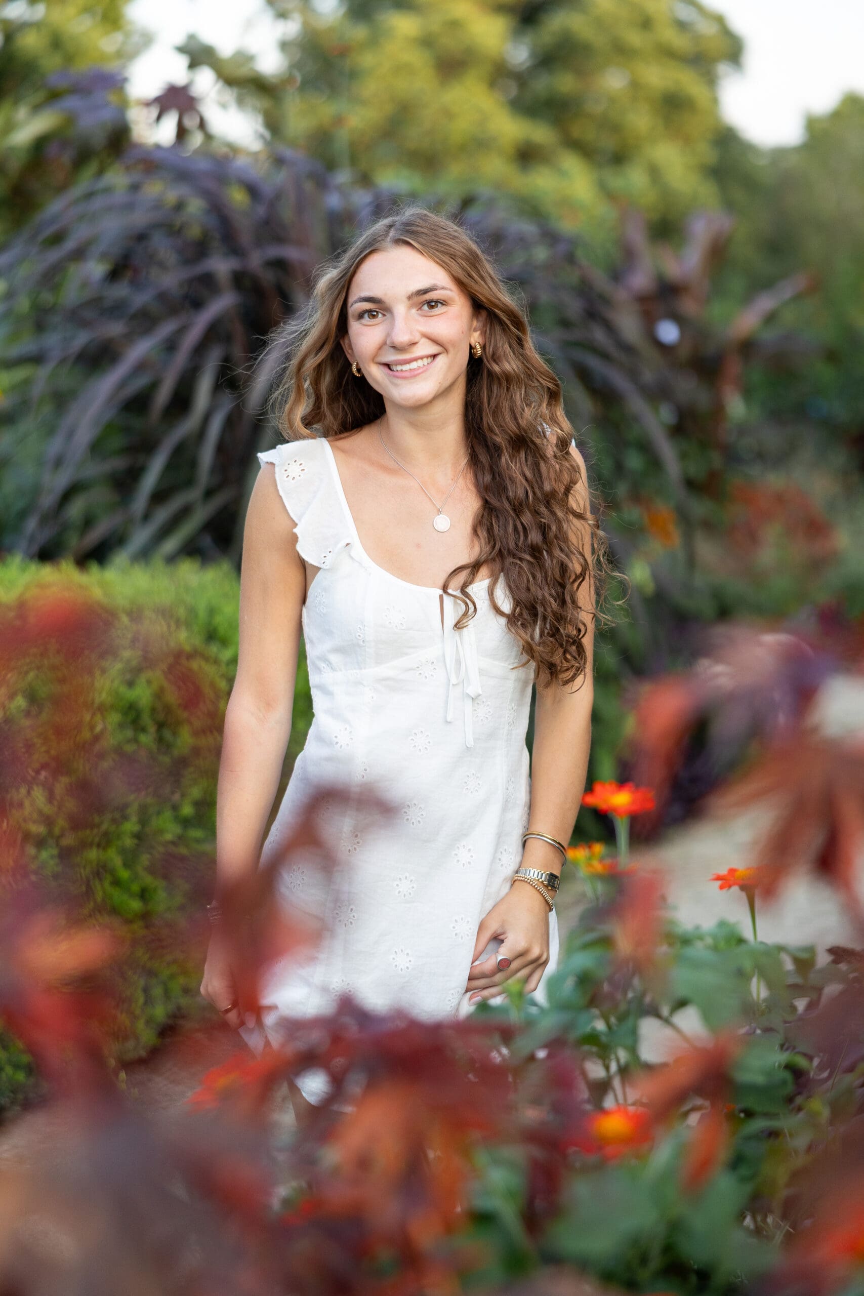 Girl wearing a beautiful white dress posing in front of pretty red flowers. 