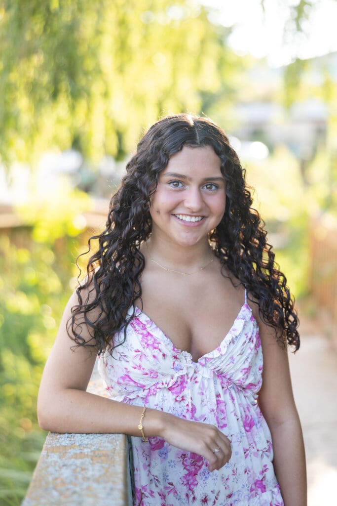 Beautiful young lady with curly brown hair smiling on a bridge during her senior session.