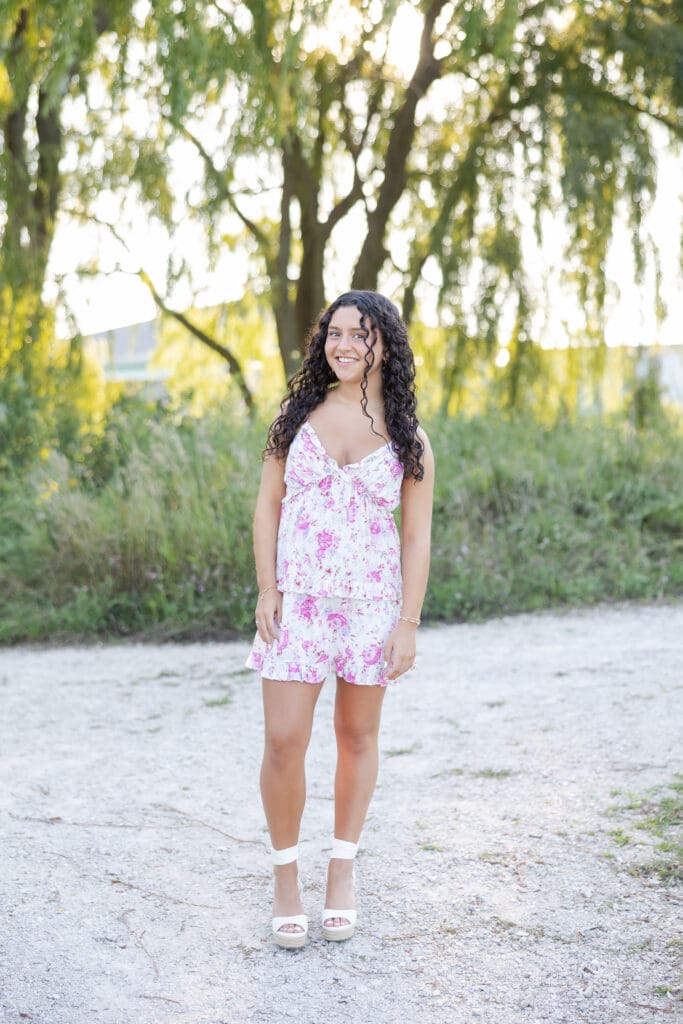 A young woman in a floral dress surrounded by a beautiful green backdrop.