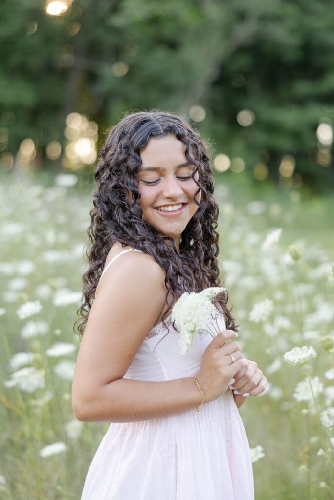 Senior in highschool holding white flowers and smiling at the camera.