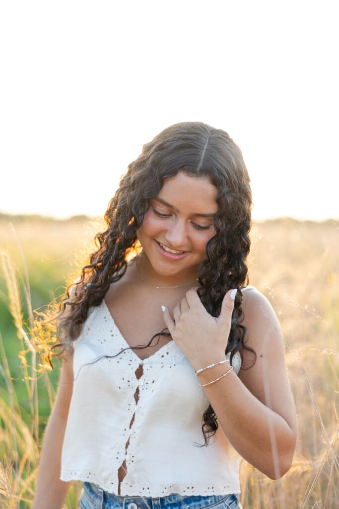 A girl holding her beautiful curly hair in a field in a fall senior session.