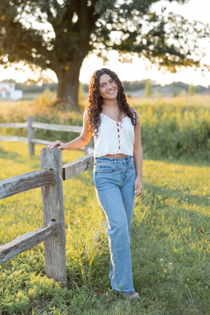 A girl smiling during her senior session, leaning against a wooden fence.
