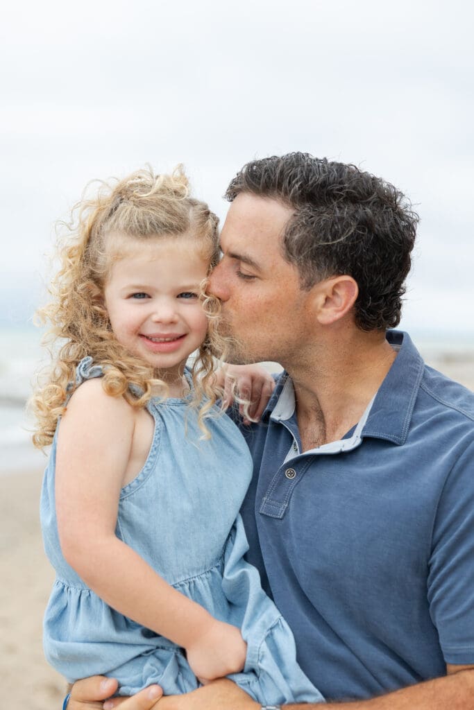 Father kissing his young daughters cheek, during a photography session on the beach. 