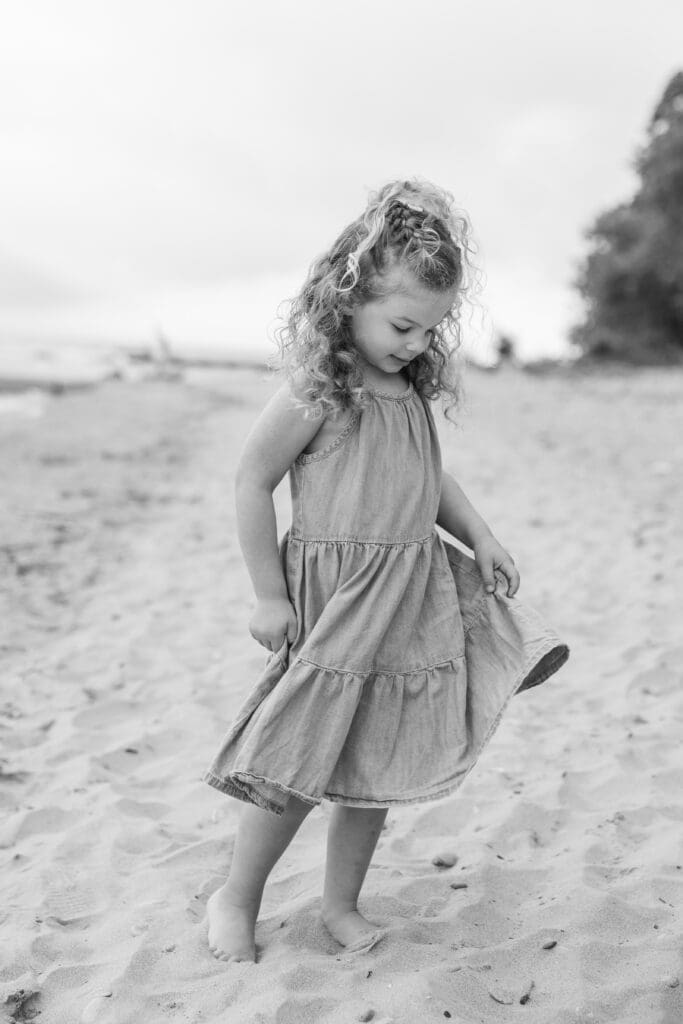 Young girl holding her dress and twirling on the beach.