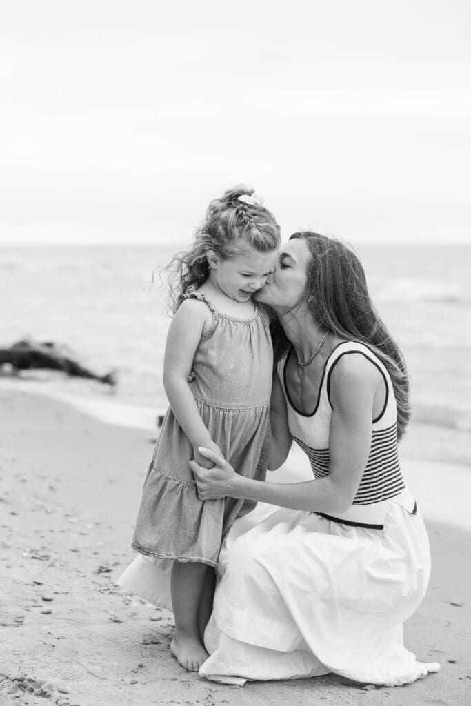 Mother kissing her daughter on the cheek while on the beach at Lake Milchigan.  