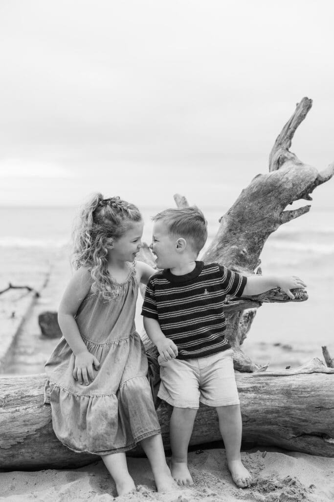 Brother and sister sitting on a tree stump face to face laughing and smiling together. 