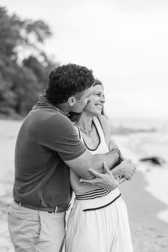 A husband and wife with their arms around one another looking at Lake Michigan in Doctors Park.  
