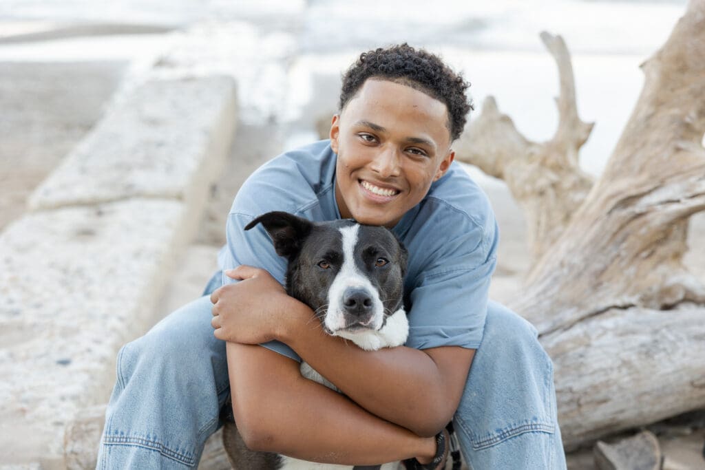 Senior in highschool hugging his dog on the beach 