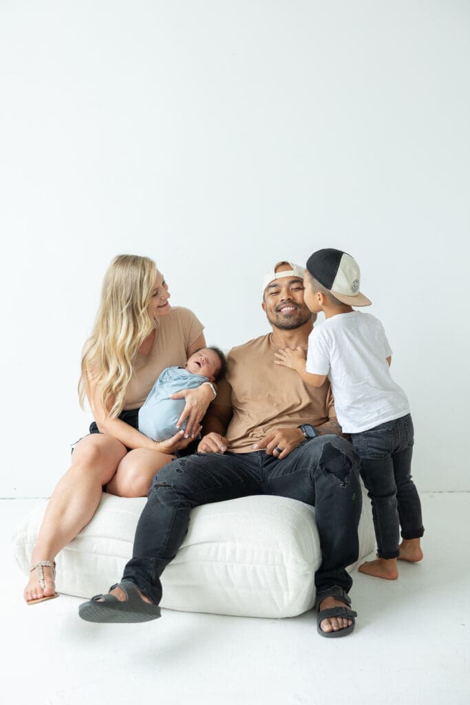 Big brother kissing Dad on the cheek while Mom is holding newborn brother for a studio photography session 