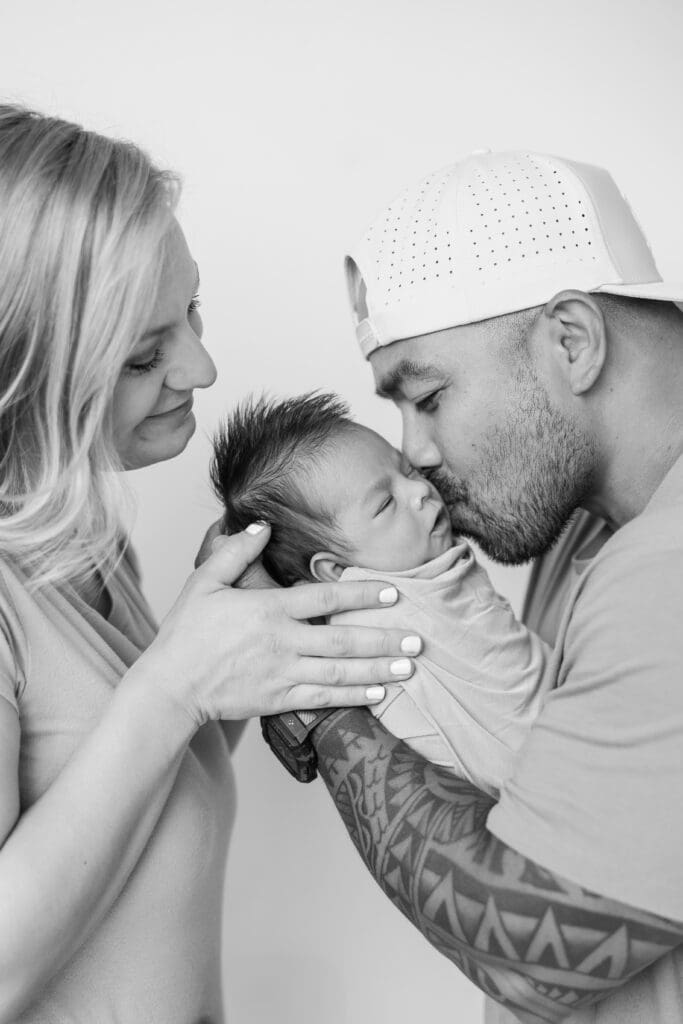Dad kissing newborn son while mother looks on 