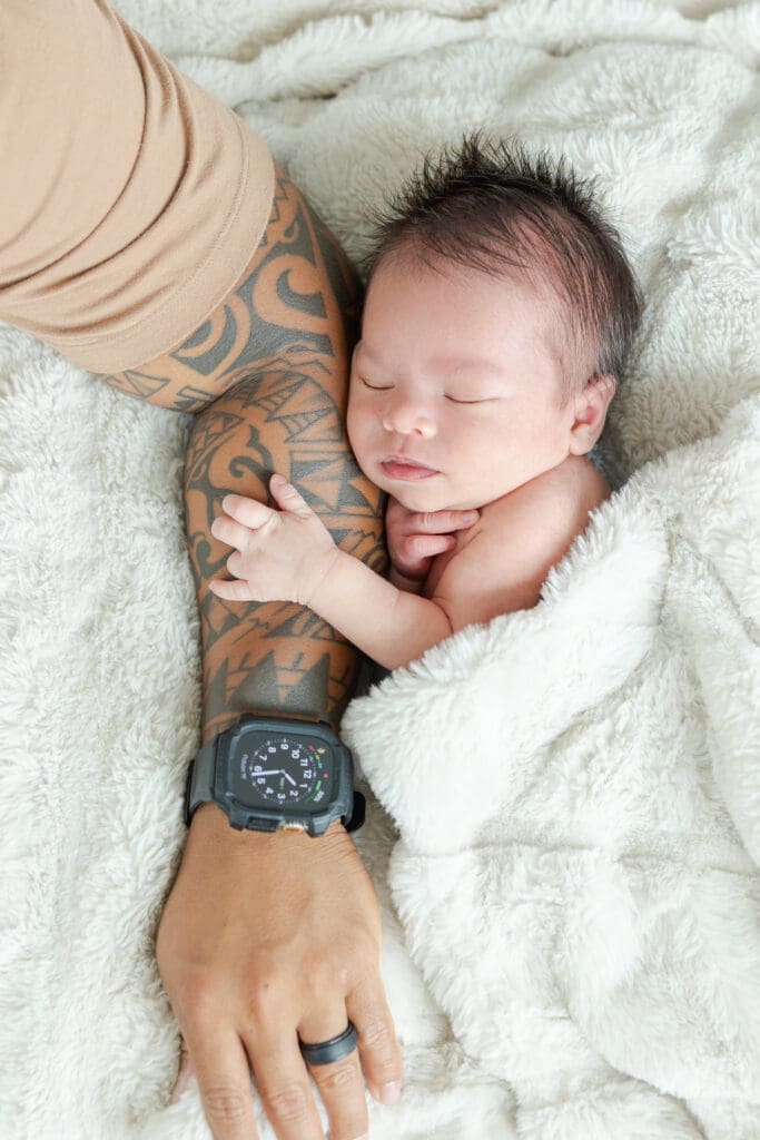 Baby with his arms wrapped around Dad's arm