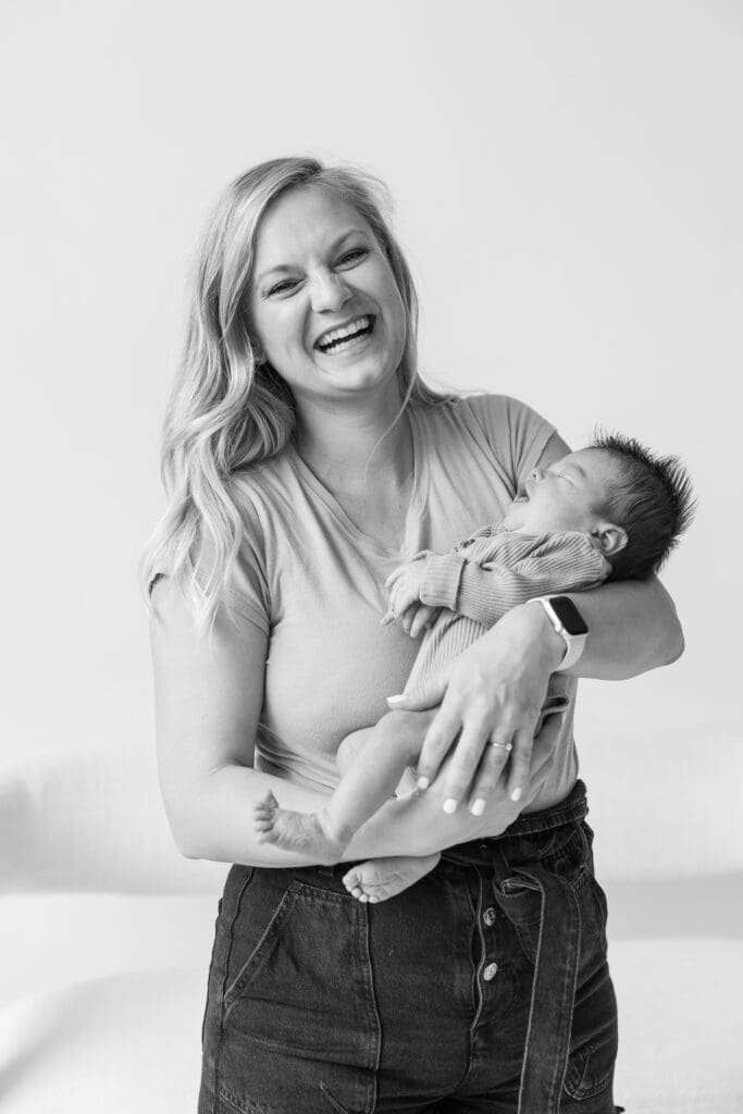 Mother holding her newborn baby boy while smiling during their newborn studio session 
